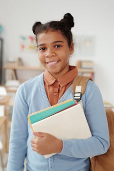 Smiling young student with a backpack and notebooks standing in a brightly lit classroom.