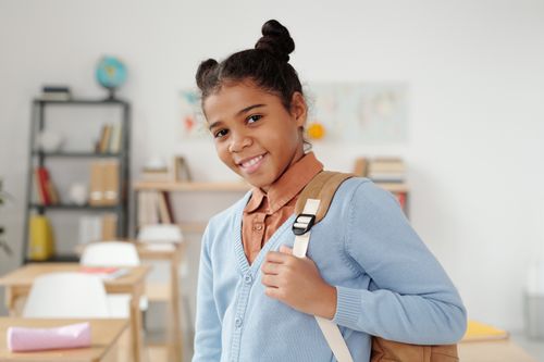Free Smiling schoolgirl wearing a blue sweater stands in a classroom, ready for school. Stock Photo