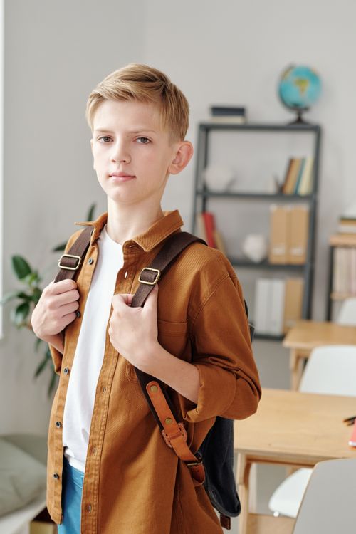 Free Blonde schoolboy with a backpack in a classroom setting, looking confident. Stock Photo