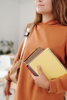 室内，一名穿着橙色连帽衫的女学生拿着笔记本，体现了教育和返校的氛围