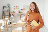 明亮的教室里，一位穿着橙色外套的开朗女学生拿着笔记本，准备迎接新学年