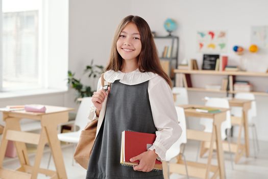 明亮的教室里，穿着校服的少女微笑着拿起笔记本