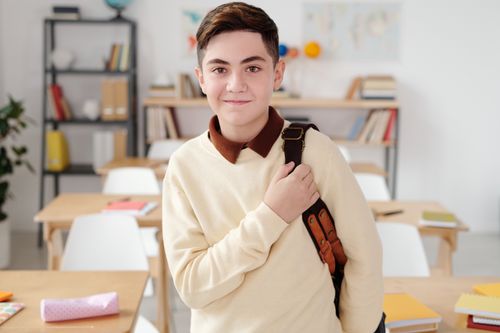 Free Smiling teenage boy with a backpack in a bright classroom setting. Stock Photo