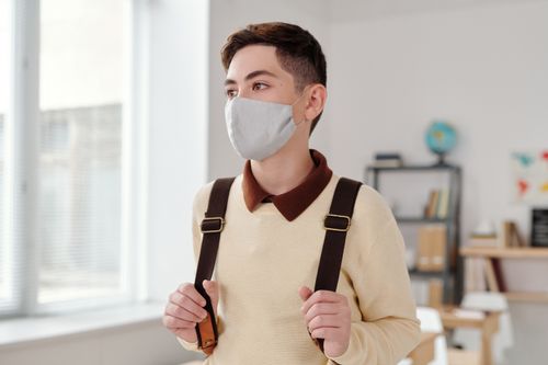 Free Portrait of a teen student wearing a face mask and backpack in a bright classroom setting. Stock Photo