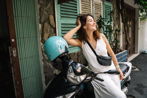 A Happy Woman in a White Dress Leaning on a Motorcycle