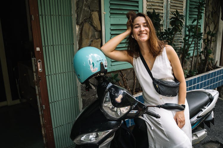 A Happy Woman In A White Dress Leaning On A Motorcycle