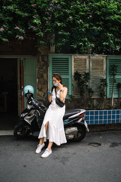 A Woman Using her Cellphone while Leaning on a Motorcycle