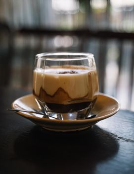 桌子上放着一个特写的玻璃杯，里面是泡沫卡布奇诺，配有碟子和茶匙