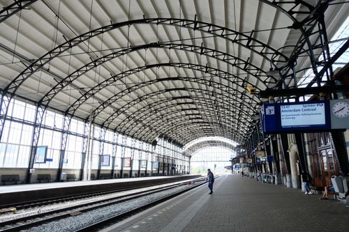 Free Amsterdam train station interior showing tracks and commuter waiting, captured during the day. Stock Photo