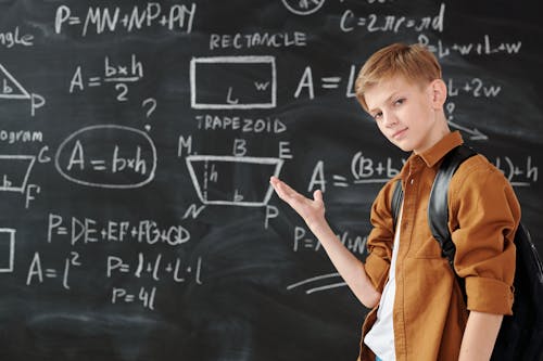 Boy in Brown Jacket Standing in Front of Chalk Board