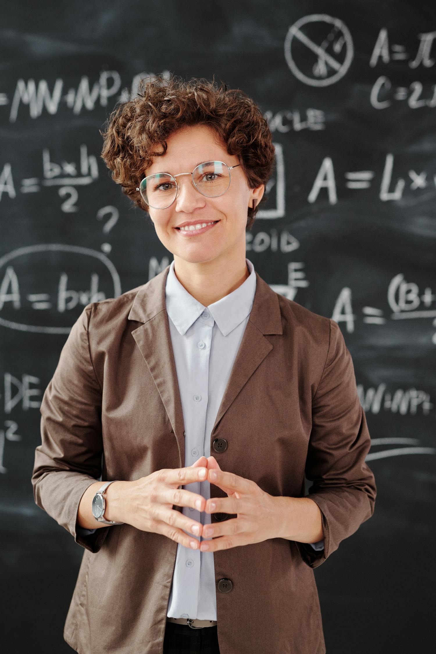 Teacher standing by a blackboard with algebra equations, smiling confidently.