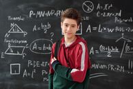 一个十几岁的男孩自信地站在写满数学公式的黑板前，展现了他对学习的热情
