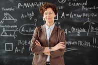 一位自信的女老师双臂交叉，站在写满详细数学内容的黑板前