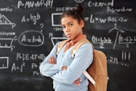 一名背着背包的非裔美国女孩自信地站在教室里写满数学的黑板前