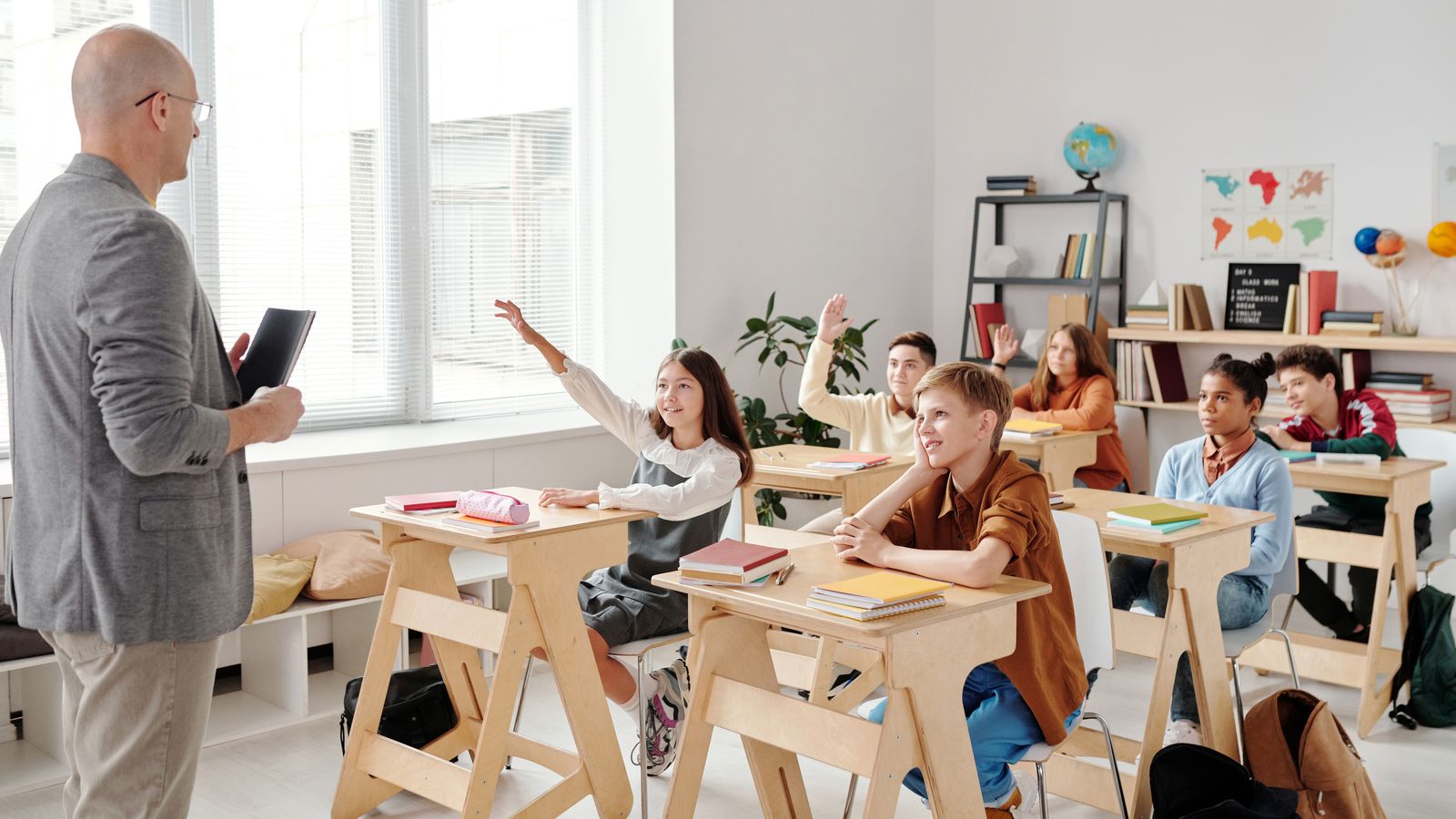 Diverse group of young students raising their hands in a classroom during a young learners TEFL lesson