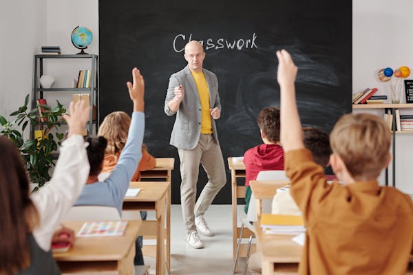 teacher looking a classroom of students with their hands raised