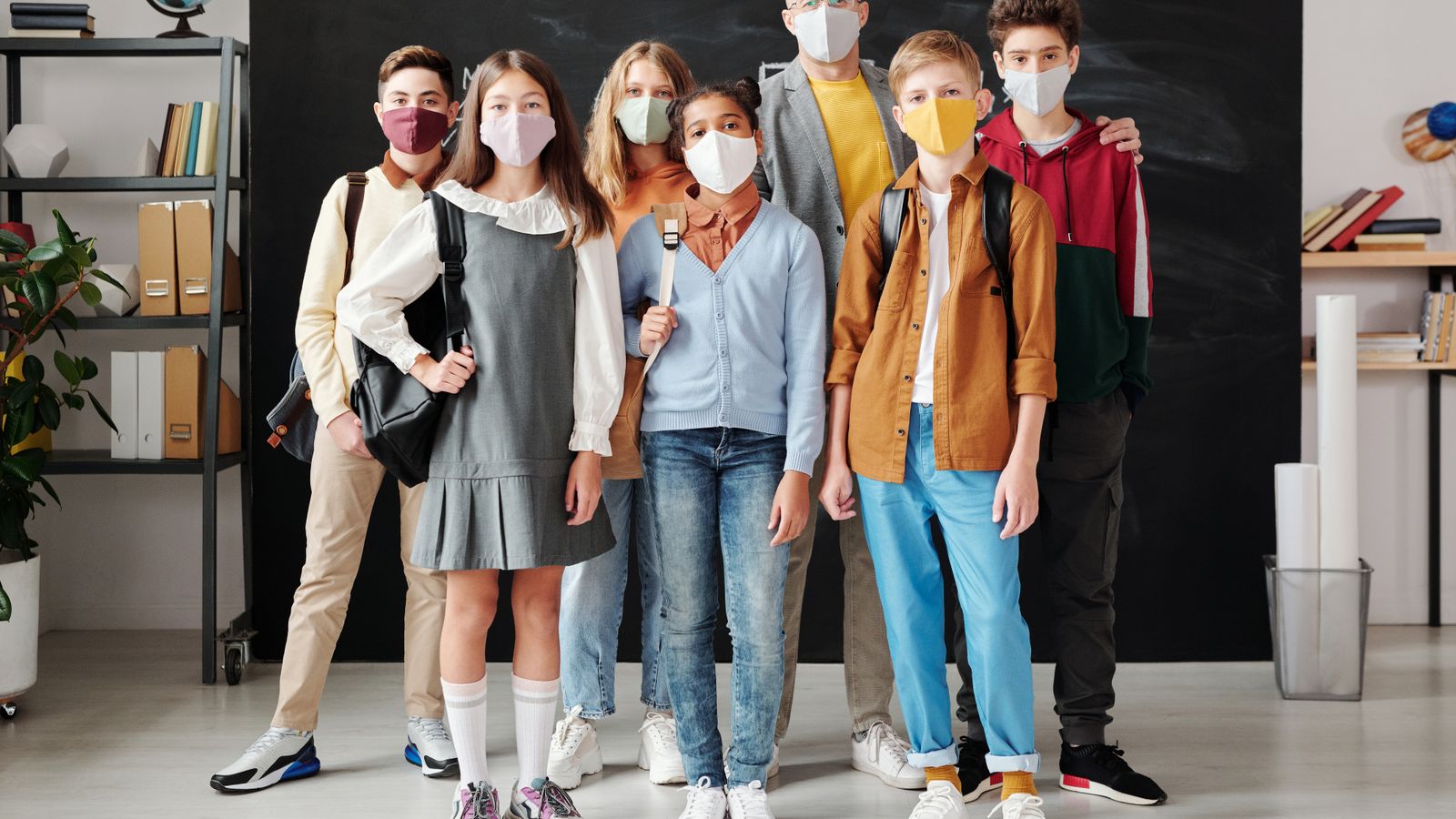 Group of students and teacher in masks standing in a classroom during the pandemic.