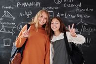 教室里，两个背着背包的学生微笑着站在数学黑板前
