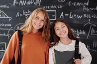 教室里，两个开朗的女孩站在数学黑板前，准备学习