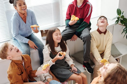 Lively group of teenagers laughing and eating pizza indoors, having a fun time together.