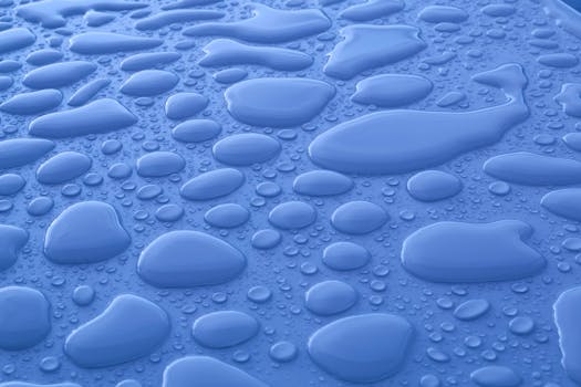 Closeup background of shiny blue surface with transparent liquid drops of different shapes