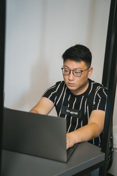 一位戴着眼镜的亚洲人正在室内专心操作笔记本电脑