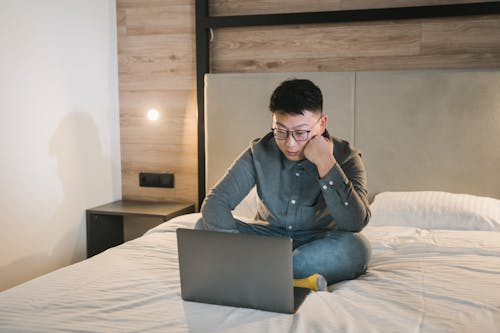 Man in Blue Denim Jacket Sitting on Bed Using Macbook