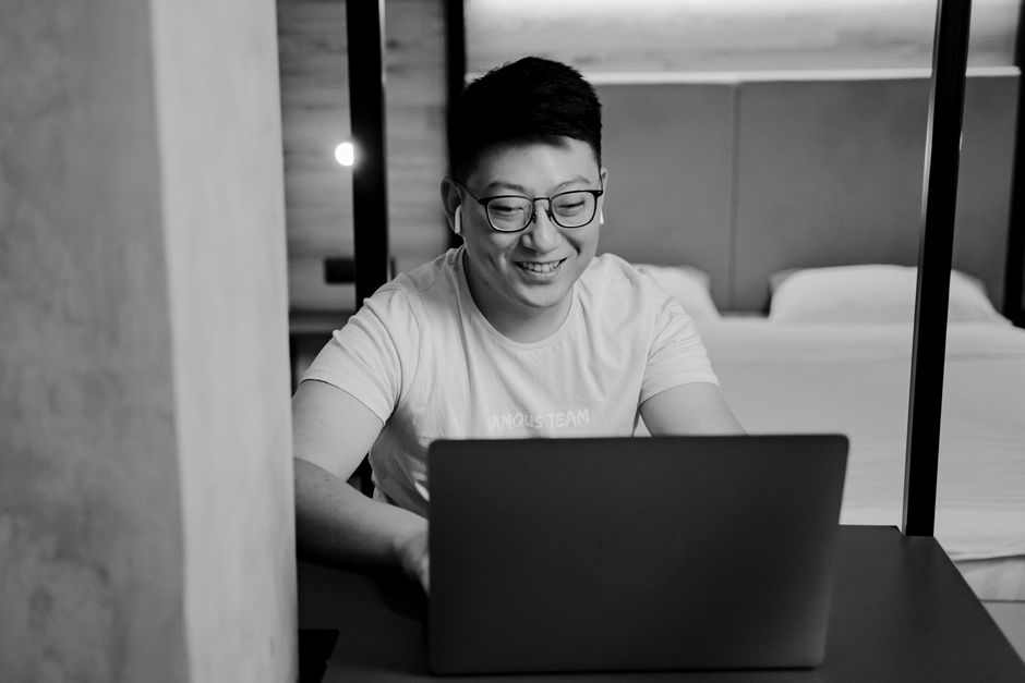 Smiling Asian man wearing glasses working on a laptop in a modern home office setting.