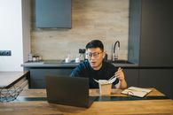 一名亚洲男子在午休时间，于现代厨房中用笔记本电脑工作，将技术融入日常生活