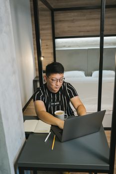 亚洲人在卧室里边喝咖啡边用笔记本电脑，专注于在线教育