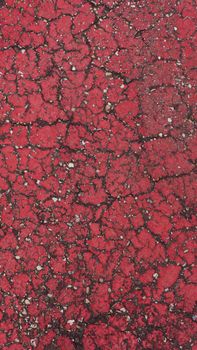 Close-up of a cracked red pavement texture outdoors, displaying rough patterns and vibrant colors.