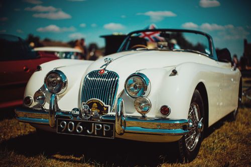 Free Luxury white shiny vintage cabriolet car parked on grassy ground against blue sky in countryside Stock Photo