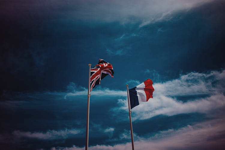 Waving Flags Of France And United Kingdom Against Blue Sky