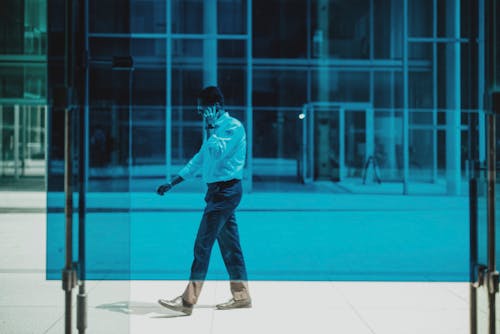 Side view of unrecognizable male entrepreneur in formal outfit walking on street near blue glass board and talking on mobile phone during break