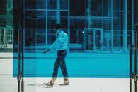 Side view of unrecognizable male entrepreneur in formal outfit walking on street near blue glass board and talking on mobile phone during break