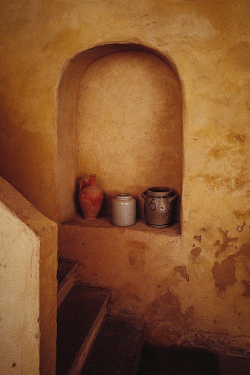 High angle of handicraft ancient clay pots placed in arched shelf in wall near staircase of aged house