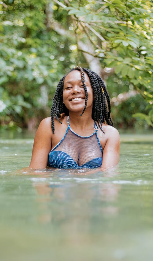 Free Young cheerful black female traveler in stylish swimwear swimming in pond during trip while looking at camera Stock Photo