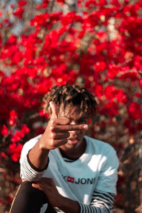 Free Selective focus of young African American indignant guy showing middle finger while resting in blooming park Stock Photo