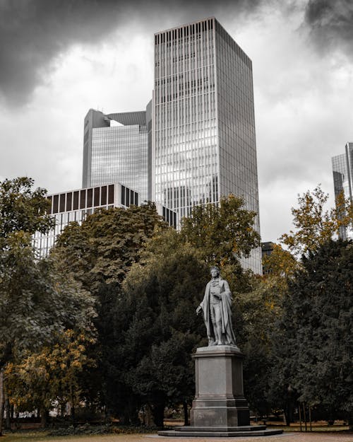 Gray Concrete Statue Near Green Trees and High Rise Buildings