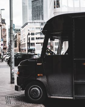 Black parcel delivery truck parked on a busy urban street in Germany, showcasing logistics and urban transportation.