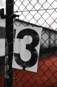 Close-up of a rustic metal fence with a large number three sign in Germany.