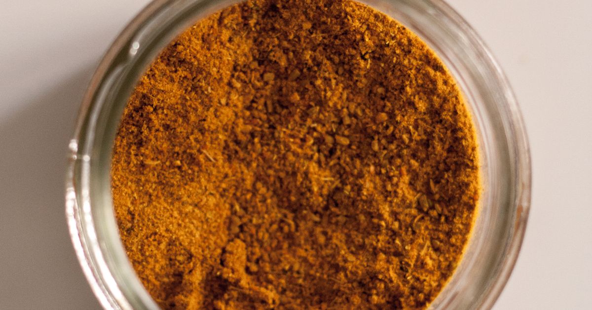 Ground turmeric in a glass bowl on a dark wooden surface