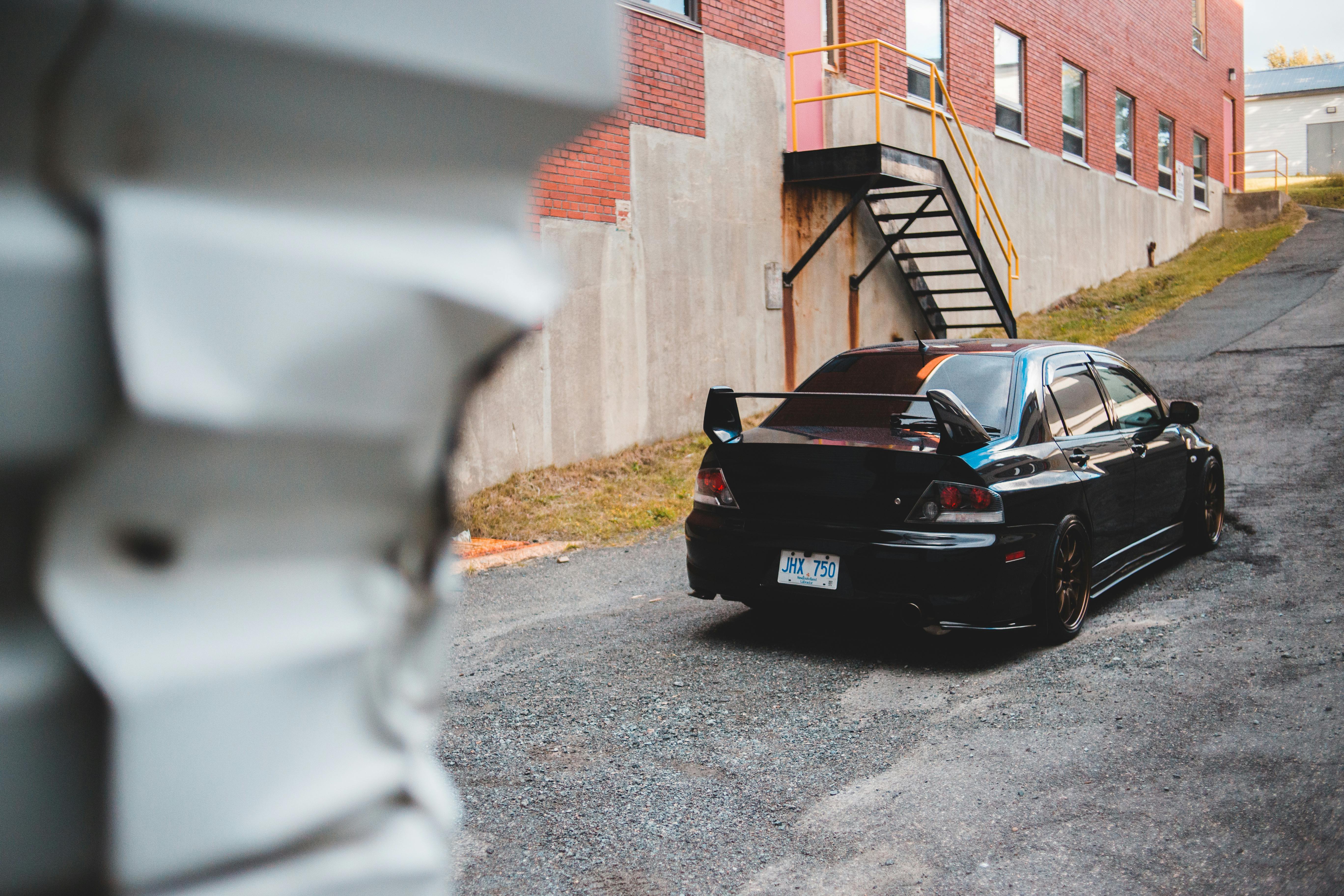 Free Rear view of a black sports car parked by a brick building with a stairway and industrial vibe. Stock Photo