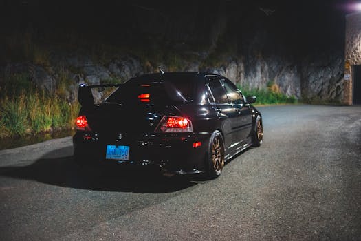 Black sport car parked on mountain path at night with illuminated taillights.