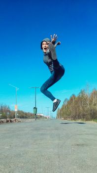 Energetic woman in midair jump on a sunny day against a clear blue sky in an outdoor setting.