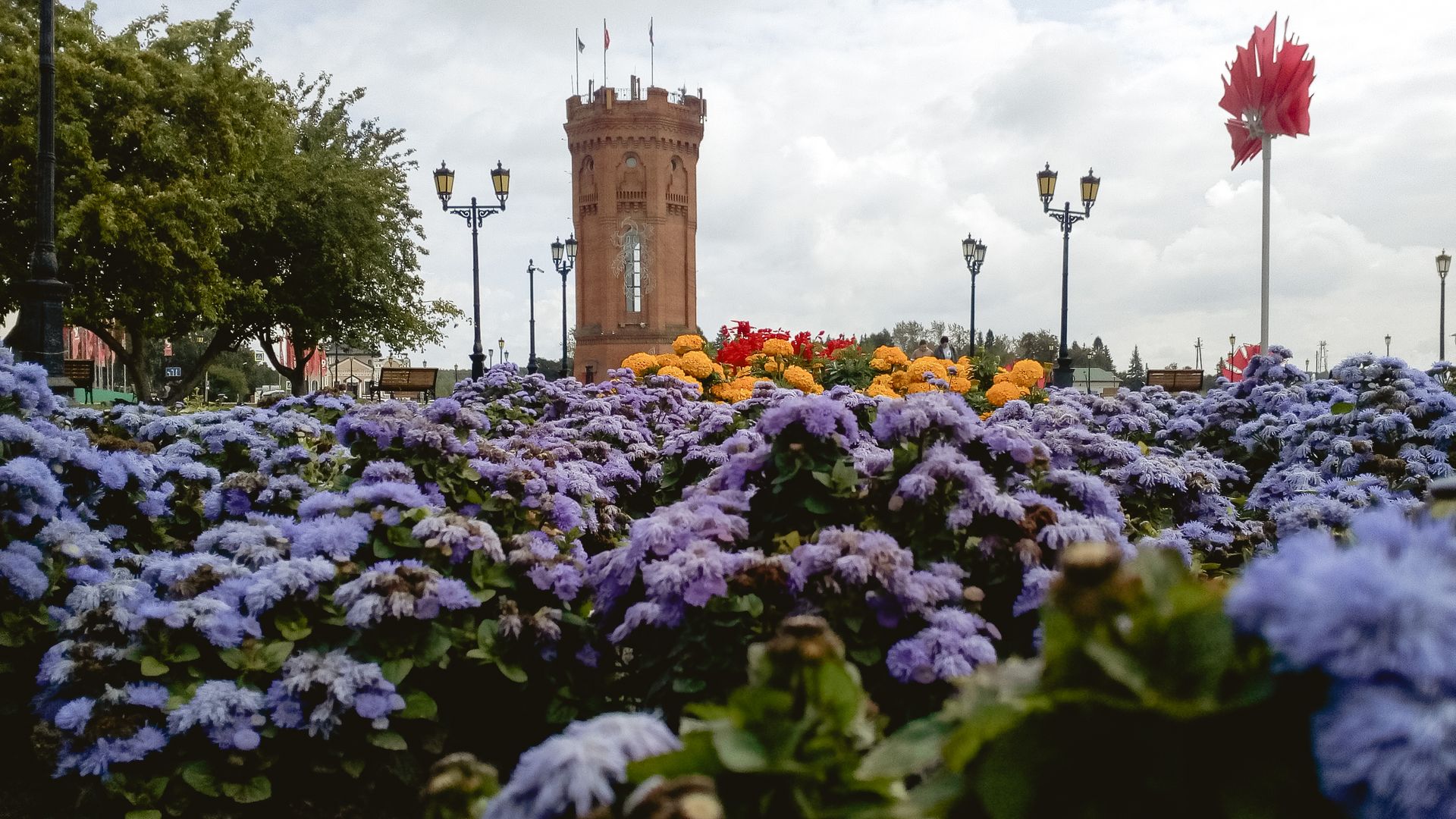 A scenic view of the Tobolsk Water Tower with lush colorful flowers under a cloudy sky in Russia.