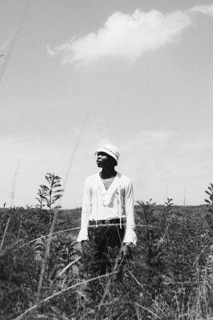 Black and white of thoughtful African American female promenading and looking away in herbal field under cloudy sky