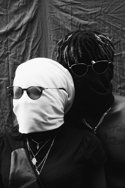Multiracial couple of anonymous faceless woman and black man wearing sunglasses and amulets on neck near black crumpled textile