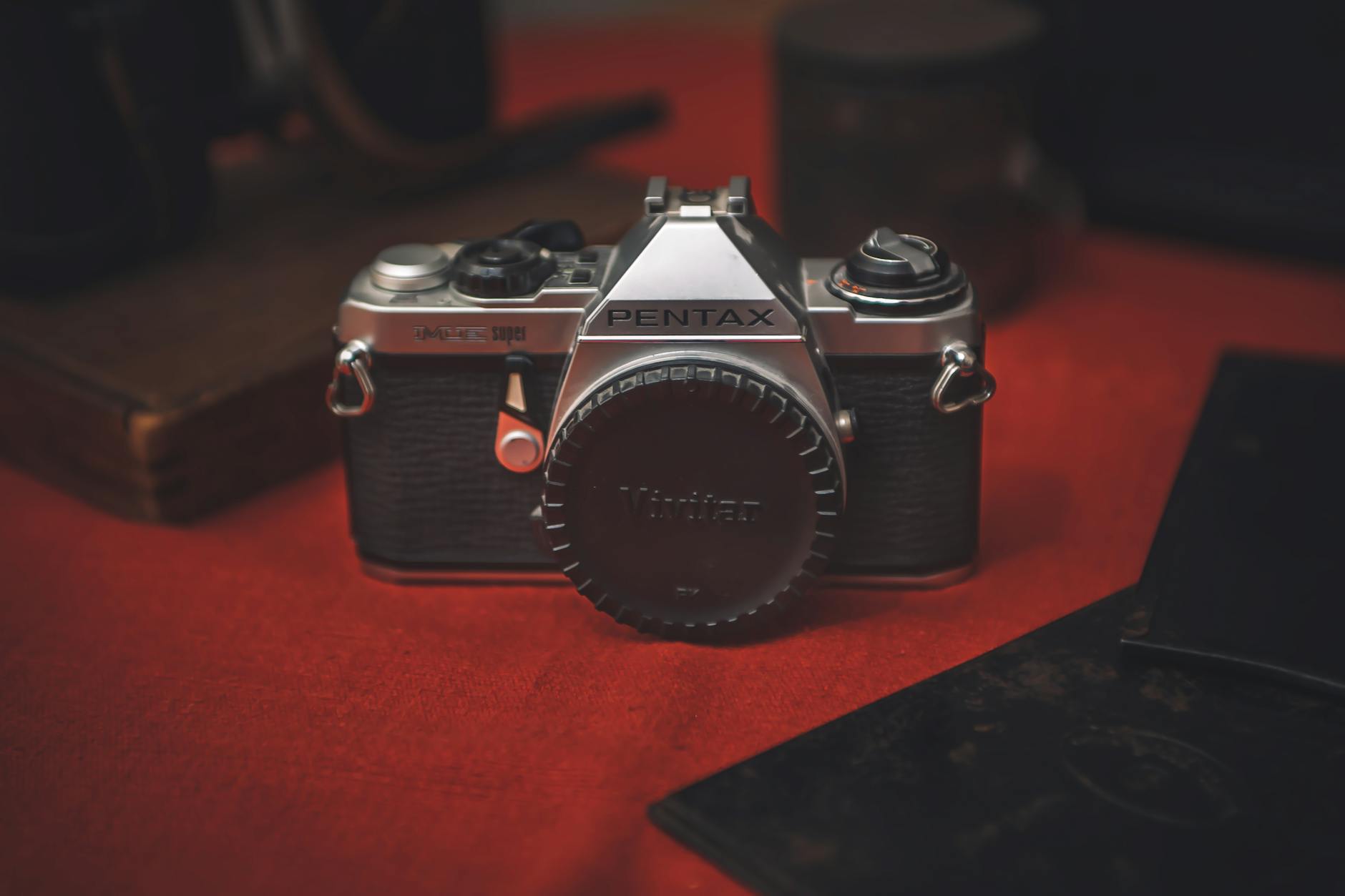 Close-up of a vintage Pentax film camera on a rustic red surface, evoking nostalgia and classic photography.