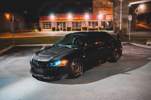 Luxury sport car with bright headlights on asphalt parking lot in illuminated city